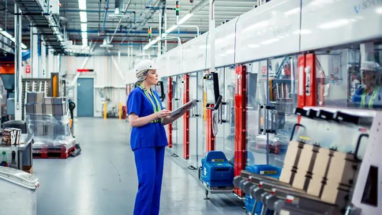 A woman in a factory holds a clipboard, overseeing operations and ensuring quality control.