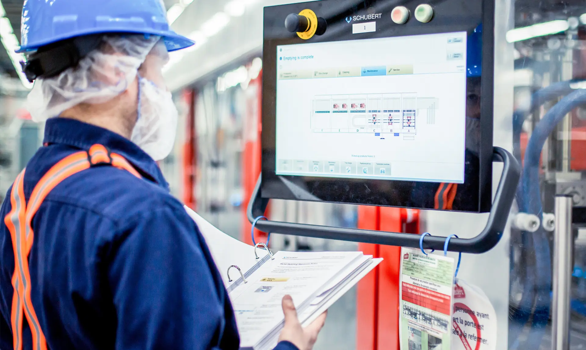 A man wearing a hard hat and safety glasses is focused on a computer screen in a work environment.