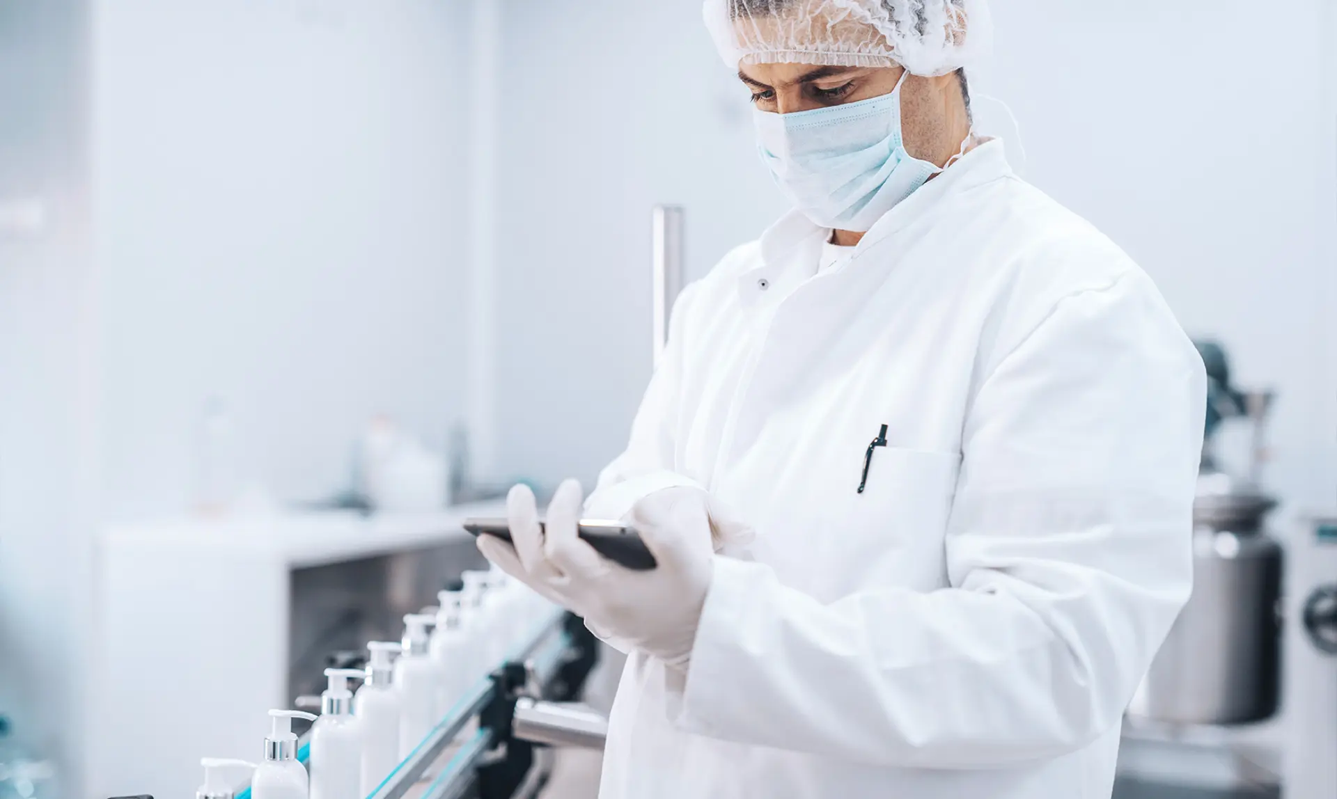 A man in a lab coat is holding a tablet while standing in a laboratory setting.