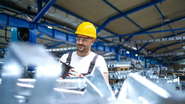 A smiling man wearing a hard hat, actively working in a factory setting.