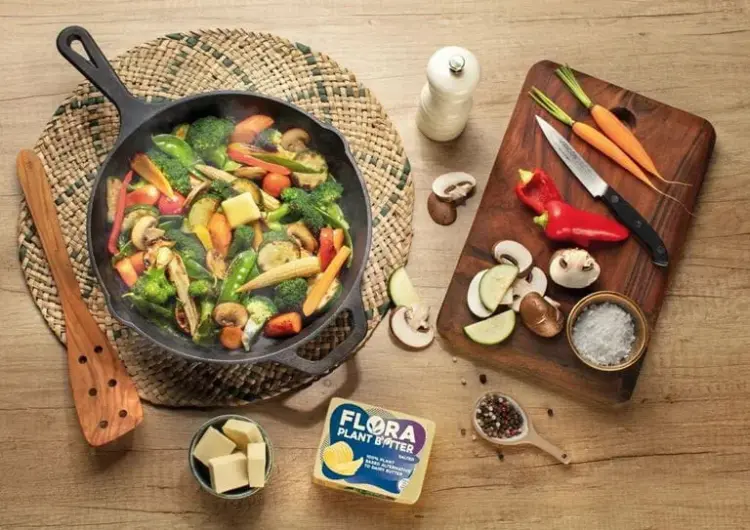 A pan filled with colorful vegetables and ingredients sits on a wooden table, ready for cooking.