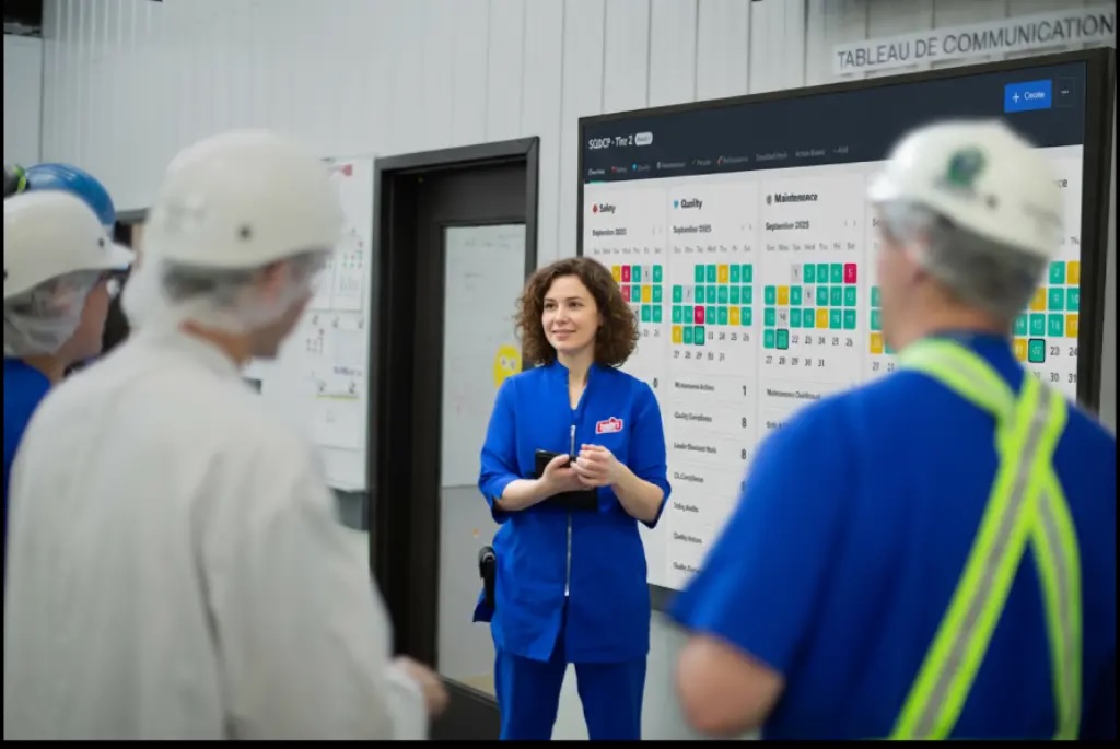 A woman in a blue and white uniform stands in front of a large screen displaying data or information.