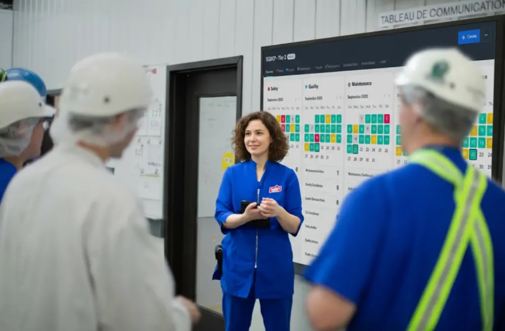 A team meeting front of a digital huddle board