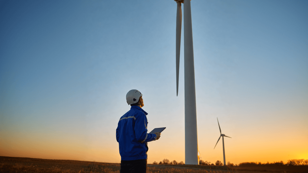 Wind turbine technician using a tablet at sunset.