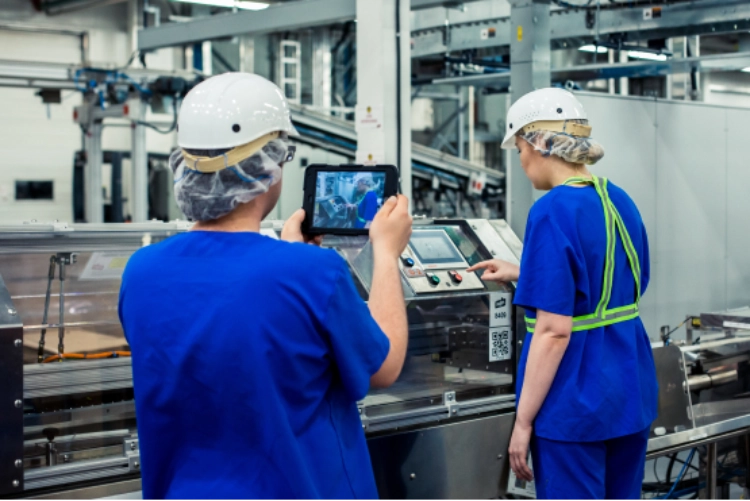A person operating a factory machinery and another person monitoring it using a mobile tablet